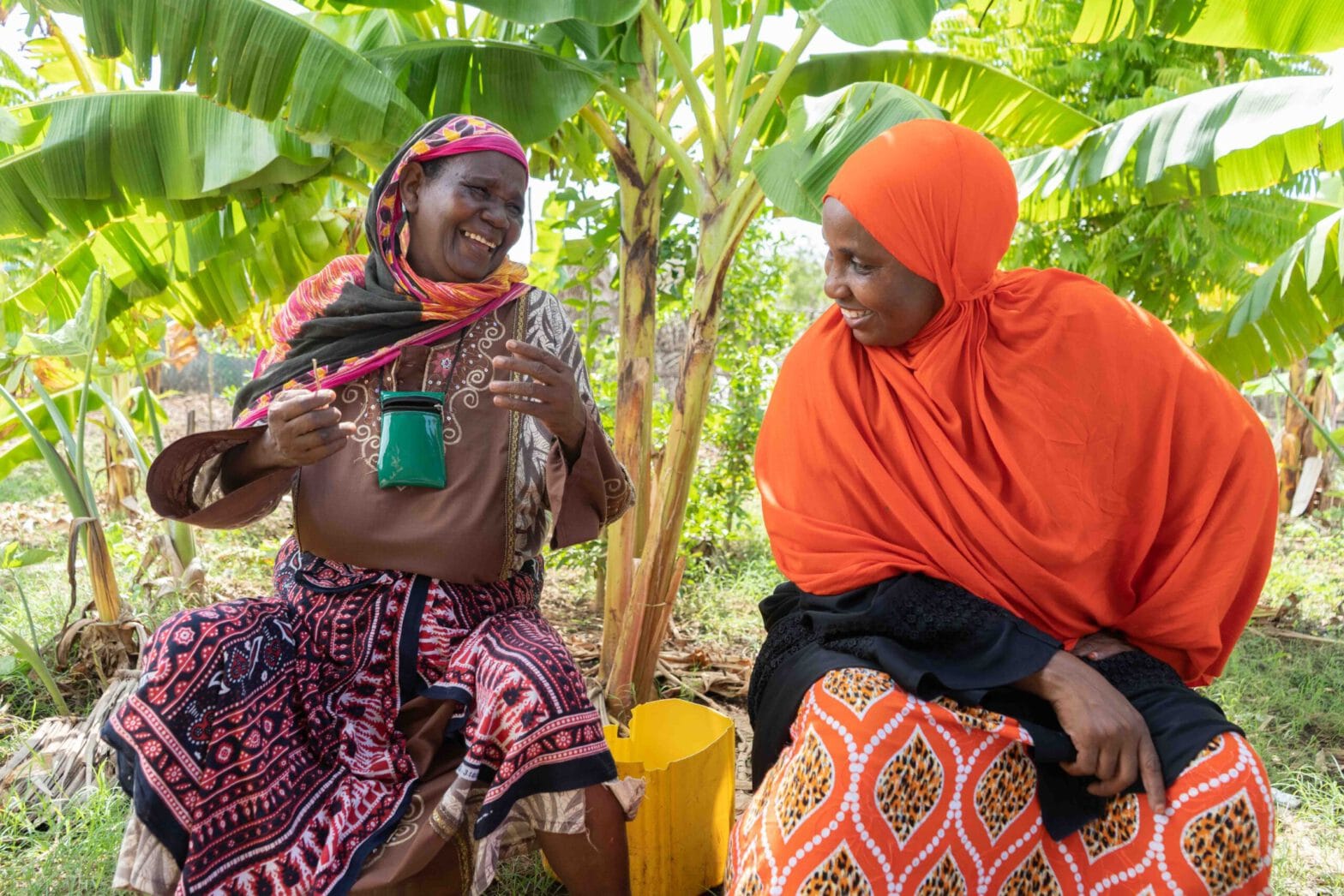 Two Pemban women laugh together in the shade of palm trees