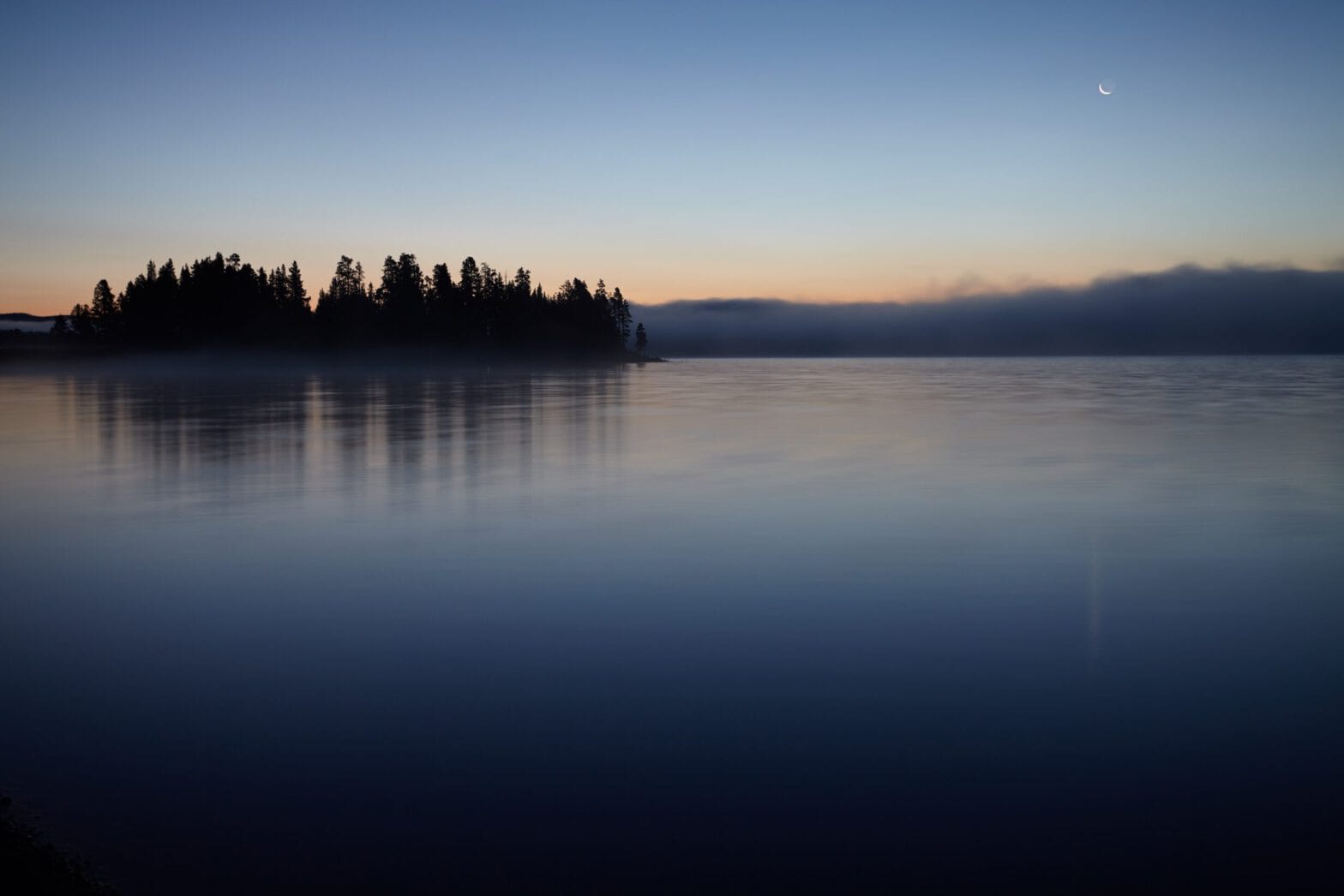 A blue lake with a small forested island at sunset.