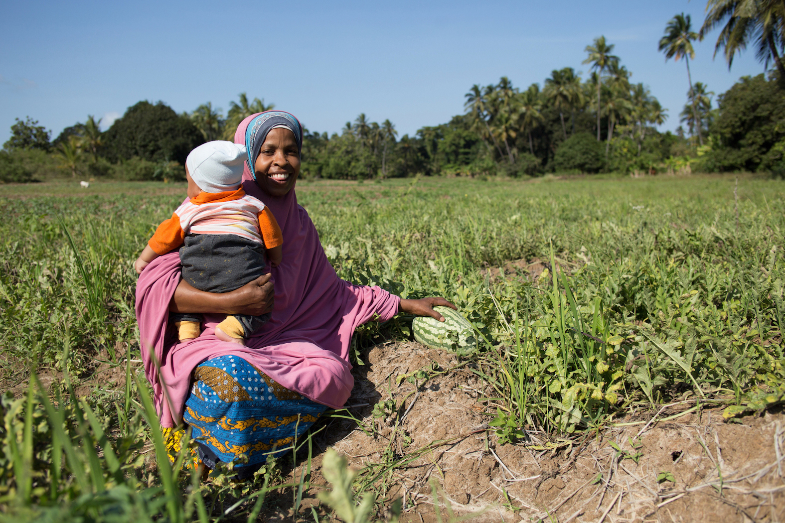 A woman holds her child in her melon patch